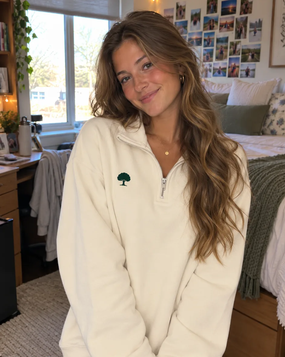 A young woman in a dorm room with string lights wearing the cream Blue Oak Cream Quarter Zip